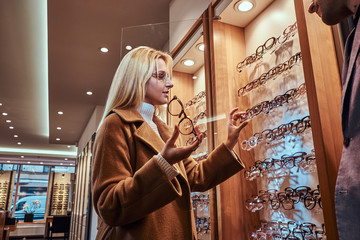 Beautiful young woman is choosing eyeglasses frame in optical store.