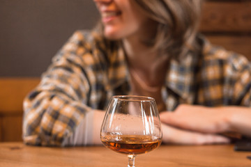 Blonde girl in a plaid shirt in a cafe with a glass of cognac.