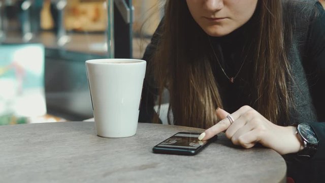 Young woman browsing on smartphone in cafe on wooden table, drinking juce. Businesswoman typing on mobile phone. 4K UHD