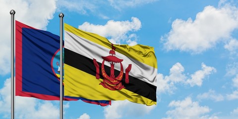 Guam and Brunei flag waving in the wind against white cloudy blue sky together. Diplomacy concept, international relations.
