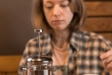 Fototapeta na wymiar Blonde girl in a plaid shirt at a table in a cafe and a glass teapot.