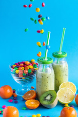 Kiwi banana and mandarin smoothie on a blue background with multi-colored sweets