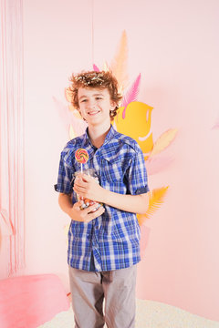 teen boy in the pool with foam soft small white balls. person engaged in relaxation therapy. caucasian kid with colorful lollipop on the stick on pink background.