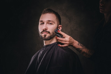 Portrait of handsome male at elite barbershop, he gets facial hair care from female.