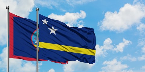 Guam and Curacao flag waving in the wind against white cloudy blue sky together. Diplomacy concept, international relations.