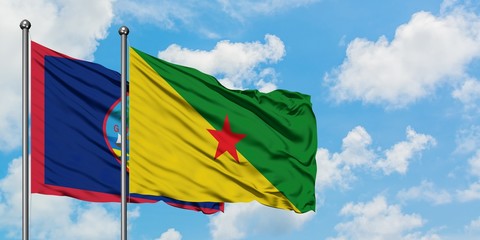 Guam and French Guiana flag waving in the wind against white cloudy blue sky together. Diplomacy concept, international relations.