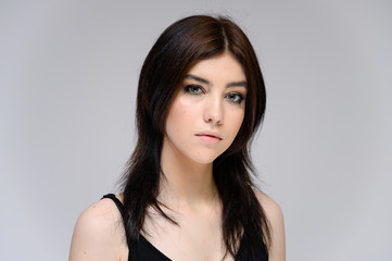Close-up portrait of a young pretty girl with long black hair, clean skin on a gray background. The concept of cosmetics for the face, great makeup, fashionable hairstyle.