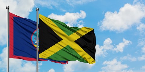 Guam and Jamaica flag waving in the wind against white cloudy blue sky together. Diplomacy concept, international relations.