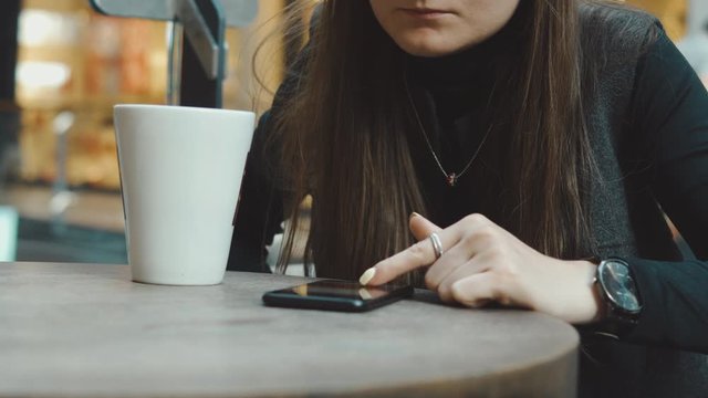 Young woman browsing on smartphone in cafe on wooden table, drinking juce. Businesswoman typing on mobile phone. 4K UHD