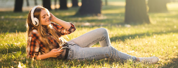 panoramic shot of beautiful girl in casual clothes lying on meadow in sunlight and listening to...