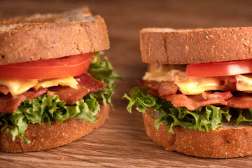 Sandwich with filling from lettuce, slices of fried bacon, tomato and cheese with whole wheat bread. wooden background. Macro photography.
