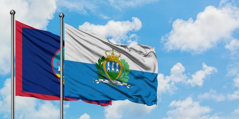 Guam and San Marino flag waving in the wind against white cloudy blue sky together. Diplomacy concept, international relations.