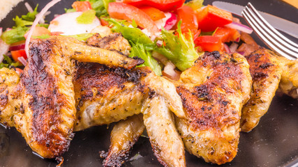 Tasty fried chicken wings with vegetable salad on a dark plate close-up
