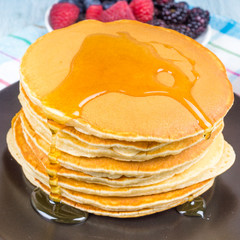 A stack of pancakes with berries and maple syrup close-up on a dark plate