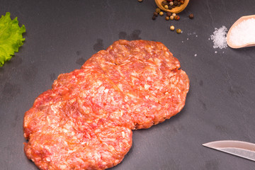 Culinary background, raw burger patties on a dark background with ingredients - salt, pepper and chopped vegetables