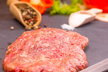 Culinary background, raw burger patties on a dark background with ingredients - salt, pepper and chopped vegetables