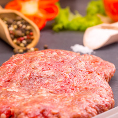 Culinary background, raw burger patties on a dark background with ingredients - salt, pepper and chopped vegetables
