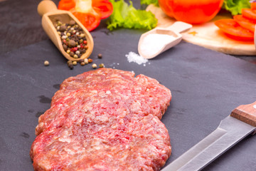 Culinary background, raw burger patties on a dark background with ingredients - salt, pepper and...