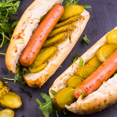 Tasty homemade buns with sausages, pickles and arugula close-up