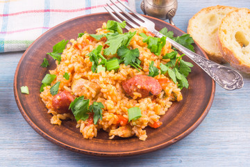 Traditional American New Orleans Jumbalaya with rice, chicken and sausages, on a clay plate, sprinkled with chopped parsley, closeup, top view.