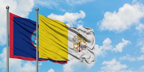 Guam and Vatican City flag waving in the wind against white cloudy blue sky together. Diplomacy concept, international relations.