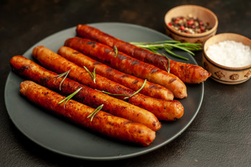 Grilled sausages on a plate with spices and rosemary on a stone table