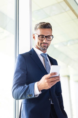 Fototapeta premium handsome businessman in formal wear and glasses using smartphone