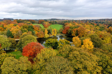 Top down aerial photo in autumn showing the beautiful fall autumn colours of a park and pond opposite a golf course in Leeds known as The Roundhay Park in West Yorkshire UK, typical British park