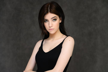 Close-up portrait of a young pretty girl student with long black hair, on a gray background. He stands right in front of the camera, showing his hands in different poses with different emotions.