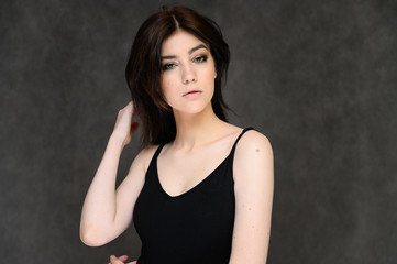 Close-up portrait of a young pretty girl student with long black hair, on a gray background. He stands right in front of the camera, showing his hands in different poses with different emotions.