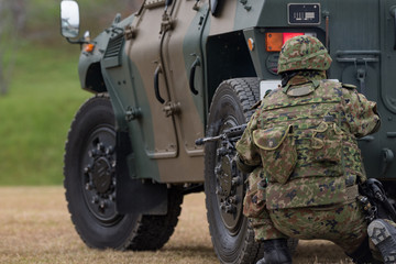 装甲車の陰で銃を構える自衛官