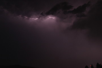 Lightning between clouds at dark night purple sky