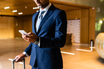 cropped view of businessman in suit using smartphone in hotel