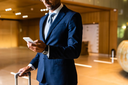 cropped view of businessman in suit using smartphone in hotel