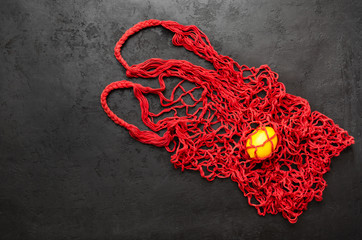 Trendy mesh net bag - alternative to plastic bags. Single yellow lemon in red reusable string bag on black background. Zero waste shopping concept. Eco friendly lifestyle. Copy space. Top view