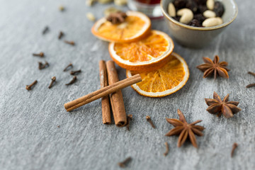 Obraz na płótnie Canvas christmas and seasonal drinks concept - cinnamon sticks, dry orange slices and star anise for hot mulled wine on grey background