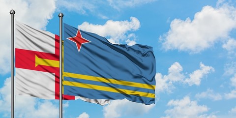 Guernsey and Aruba flag waving in the wind against white cloudy blue sky together. Diplomacy concept, international relations.