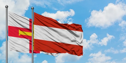 Guernsey and Austria flag waving in the wind against white cloudy blue sky together. Diplomacy concept, international relations.