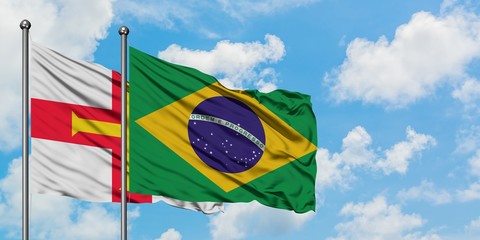Guernsey and Brazil flag waving in the wind against white cloudy blue sky together. Diplomacy concept, international relations.