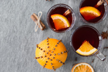 christmas and seasonal drinks concept - hot mulled wine, dry orange slices, raisins with cashew nuts and aromatic spices on grey background