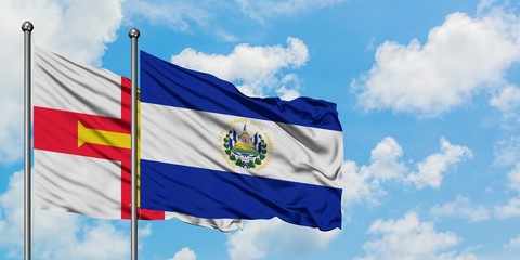 Guernsey and El Salvador flag waving in the wind against white cloudy blue sky together. Diplomacy concept, international relations.