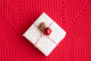 Christmas gift decorated with Christmas red ball and natural cone on red Knitting background.Merry Christmas and Napy New Year concept.