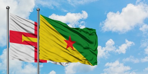Guernsey and French Guiana flag waving in the wind against white cloudy blue sky together. Diplomacy concept, international relations.