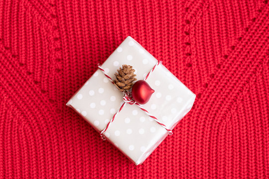 Christmas gift decorated with Christmas red ball and natural cone on red Knitting background.Merry Christmas and Napy New Year concept.
