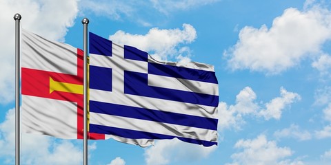 Guernsey and Greece flag waving in the wind against white cloudy blue sky together. Diplomacy...