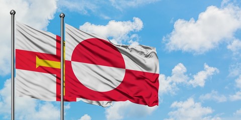 Guernsey and Greenland flag waving in the wind against white cloudy blue sky together. Diplomacy concept, international relations.
