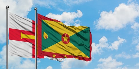 Guernsey and Grenada flag waving in the wind against white cloudy blue sky together. Diplomacy concept, international relations.