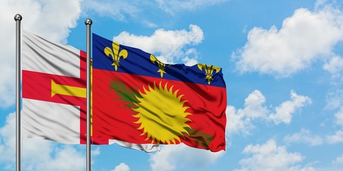 Guernsey and Guadeloupe flag waving in the wind against white cloudy blue sky together. Diplomacy concept, international relations.
