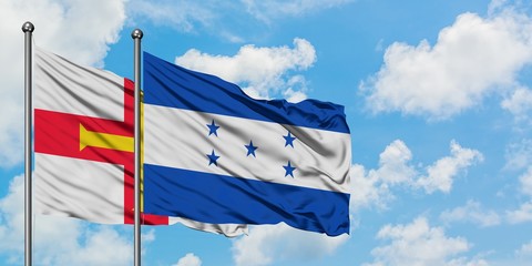 Guernsey and Honduras flag waving in the wind against white cloudy blue sky together. Diplomacy concept, international relations.