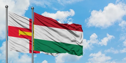Guernsey and Hungary flag waving in the wind against white cloudy blue sky together. Diplomacy concept, international relations.
